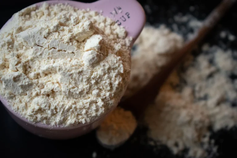 Measuring cup filled with whey protein powder on a dark surface